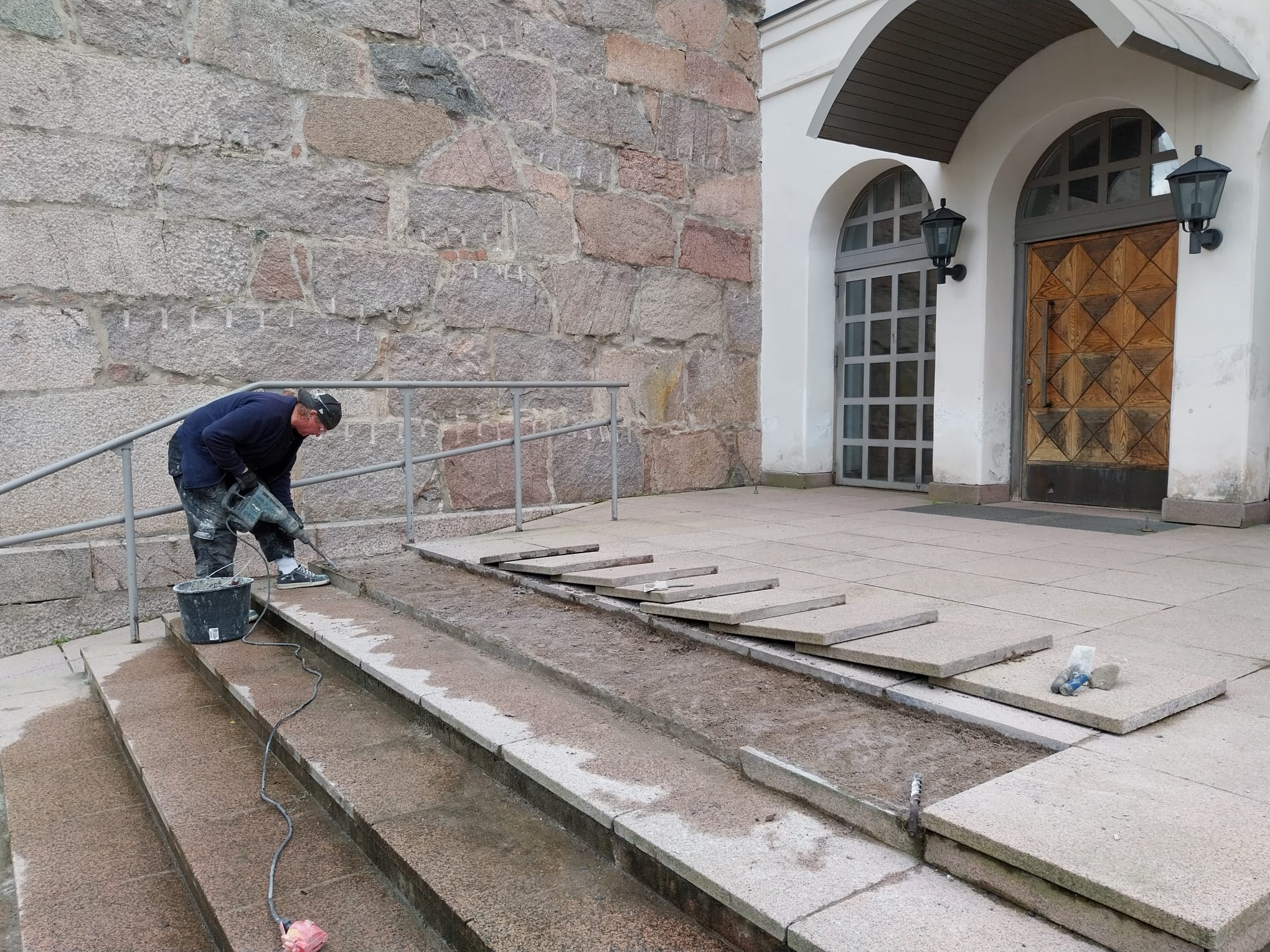 Mies irrottaa laattaa Orimattilan kirkon pääoven portaista.