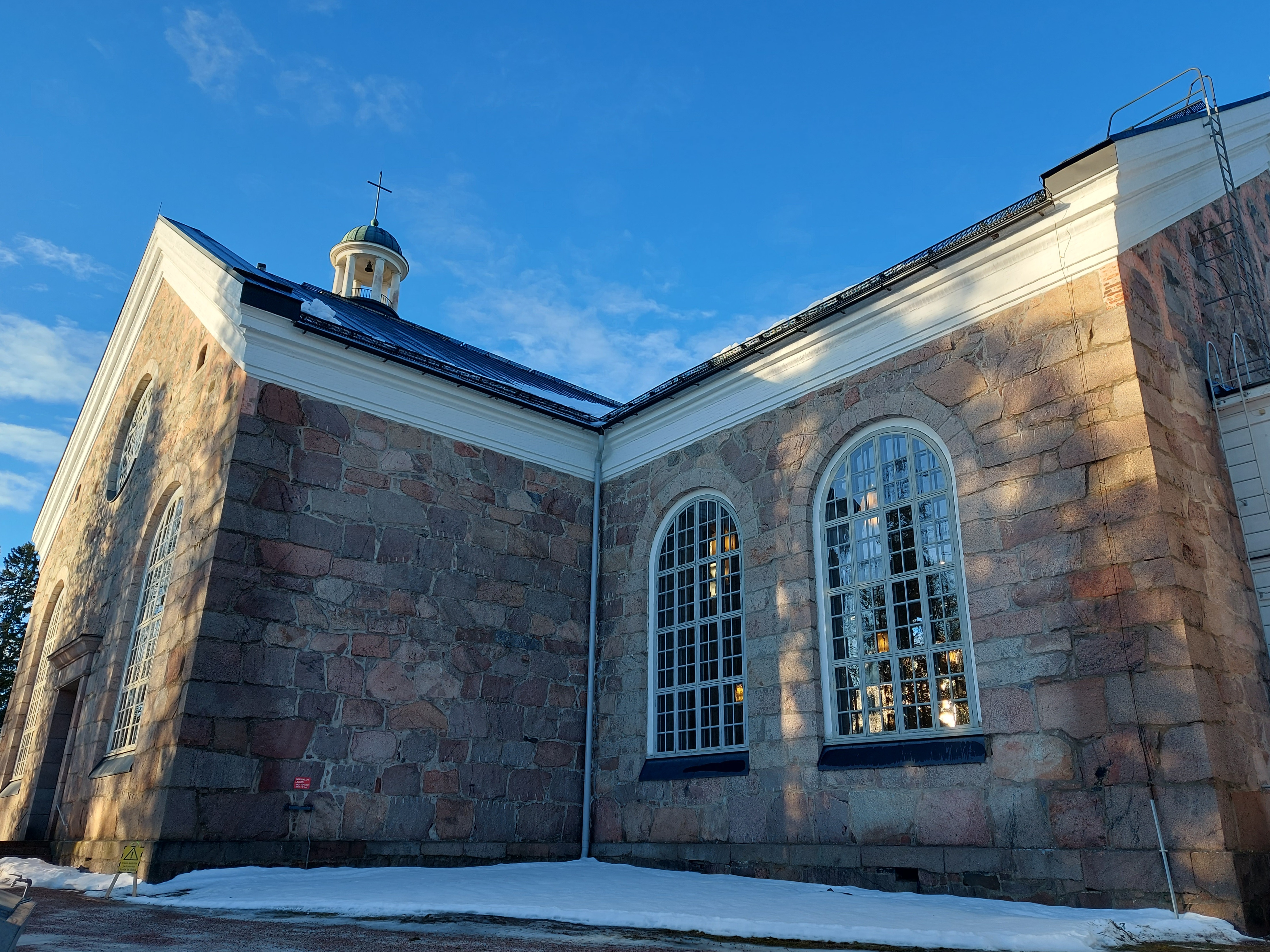 Orimattilan kirkko ulkoapäin, kirkas talvivalo heijastuu ikkunoista, sininen taivas