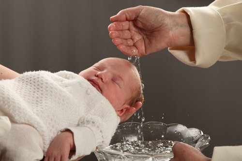 Pappi valelee vettä kastettavan vauvan pään päälle, vauva nukkuu.