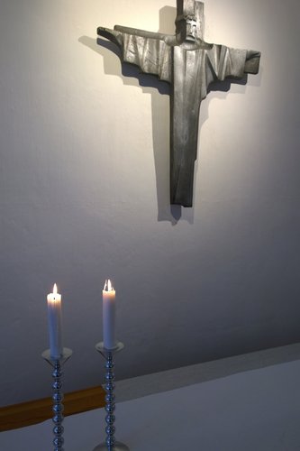 Orimattilan kirkon kappelin alttariveistos, jonka alla kaksi palavaa kynttilää alttaripöydällä.